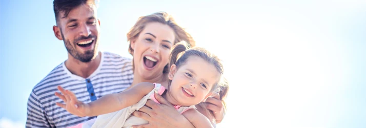 A family enjoying a bright outdoor moment, holding a child while sharing a joyful interaction.