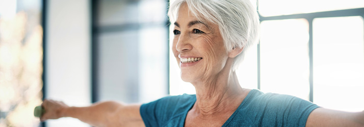 Older adult lifting light weights with arms extended, demonstrating strength and mobility training.